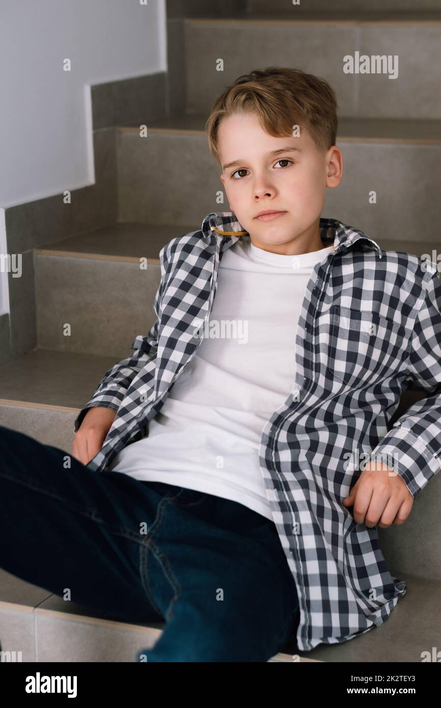 Portrait d'un adolescent mignon dans des vêtements décontractés. Un jeune homme est assis sur les marches d'un bâtiment Banque D'Images