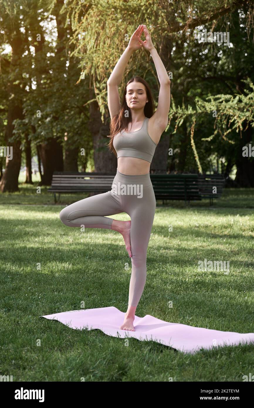 Une jeune femme positive en costume de gymnastique pratique le yoga et médite en s'asseyant sur un tapis. Banque D'Images