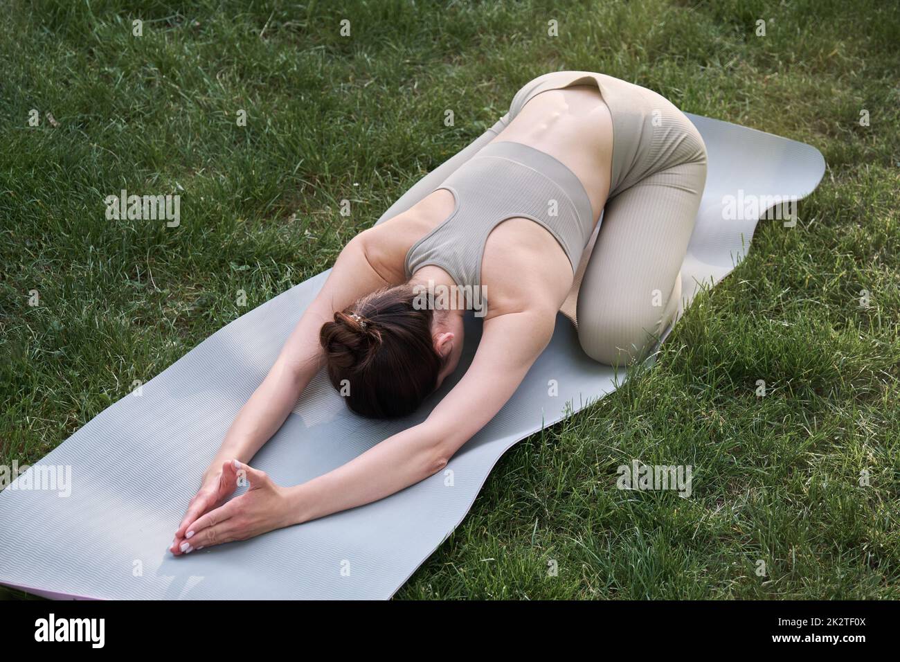 Une jeune femme pratique le yoga tout en étant allongé sur un tapis de gym. Belle fille sportive dans le parc. Banque D'Images