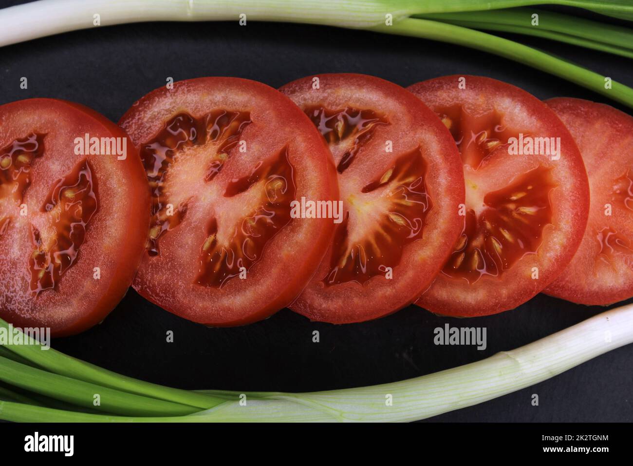 Des tranches de tomate dans un cadre d'oignons verts en gros plan sur fond noir. Le concept de saine alimentation. Banque D'Images