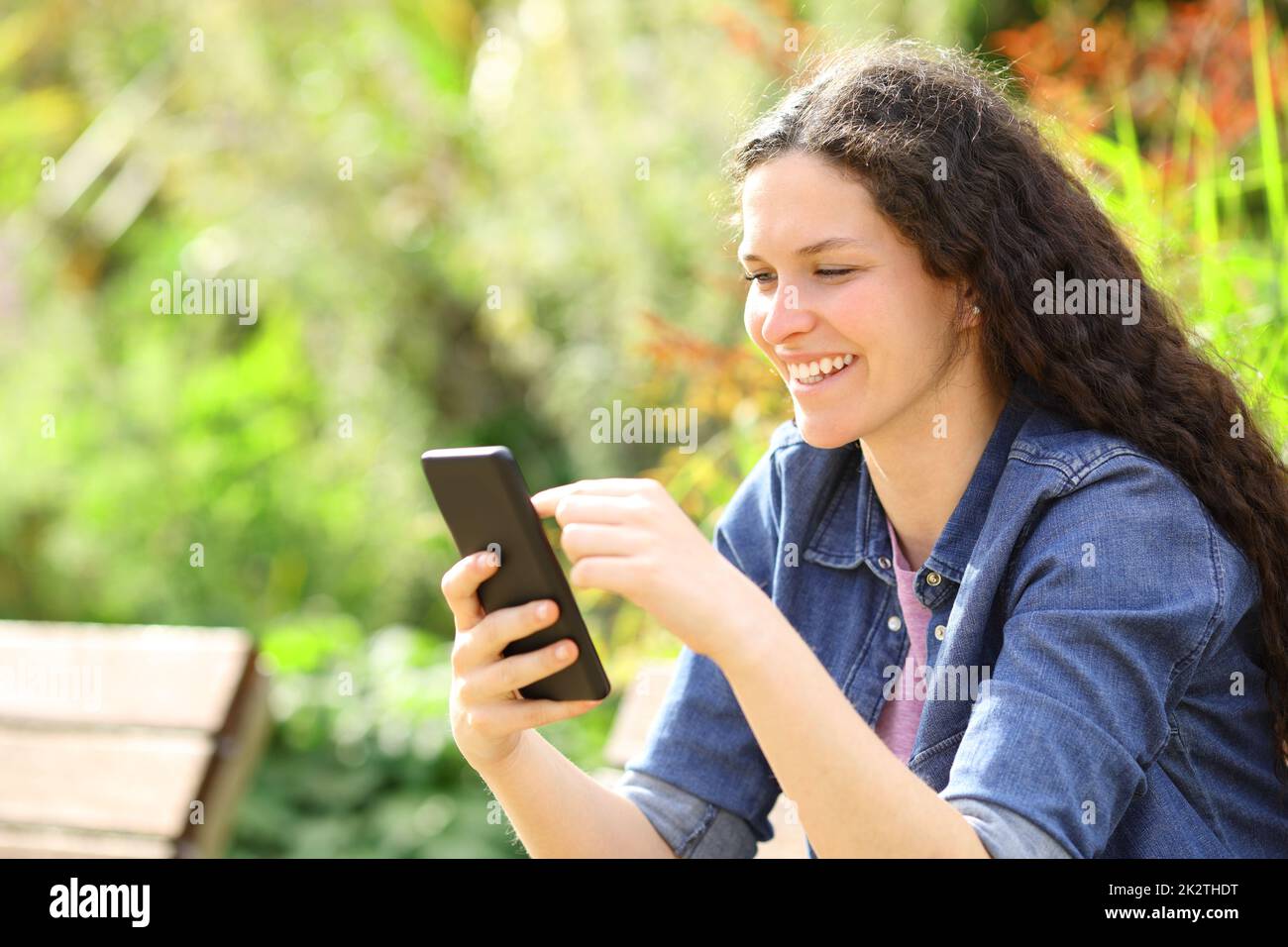 Une femme heureuse utilisant un smartphone dans un parc vert Banque D'Images