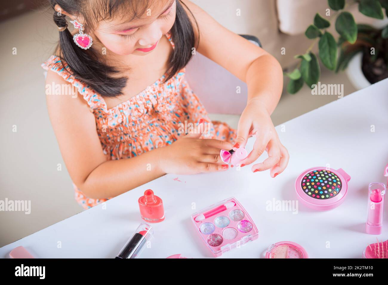 petite fille faisant le maquillage trempette brosse dans la bouteille pour peindre les ongles vernis à ongles rouge elle-même Banque D'Images