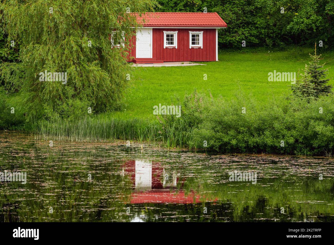 Vue sur la cabane de vacances rouge avec réflexion dans l'eau de l'étang Banque D'Images