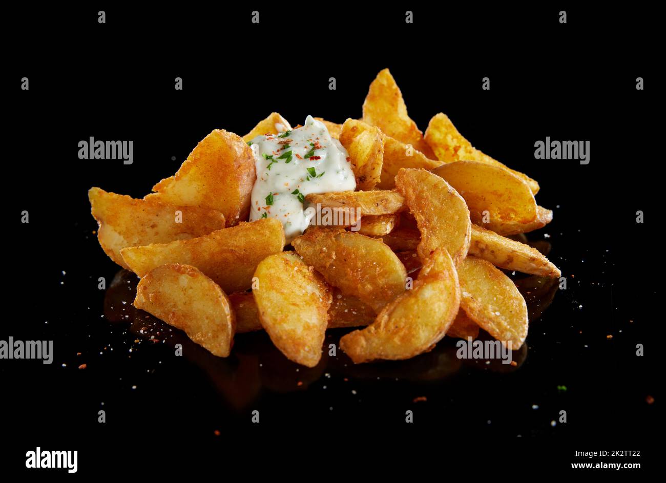 Appétissant quartiers de pommes de terre rôtis avec sauce blanche sur fond noir Banque D'Images