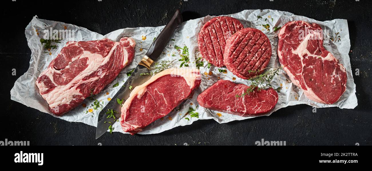 Morceaux de bœuf cru avec des côtelettes aux herbes près du couteau Banque D'Images