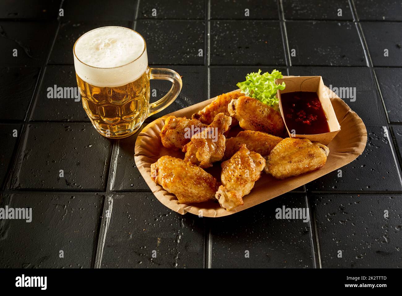 Ailes de poulet chaudes et verre de bière placé sur une table noire Banque D'Images