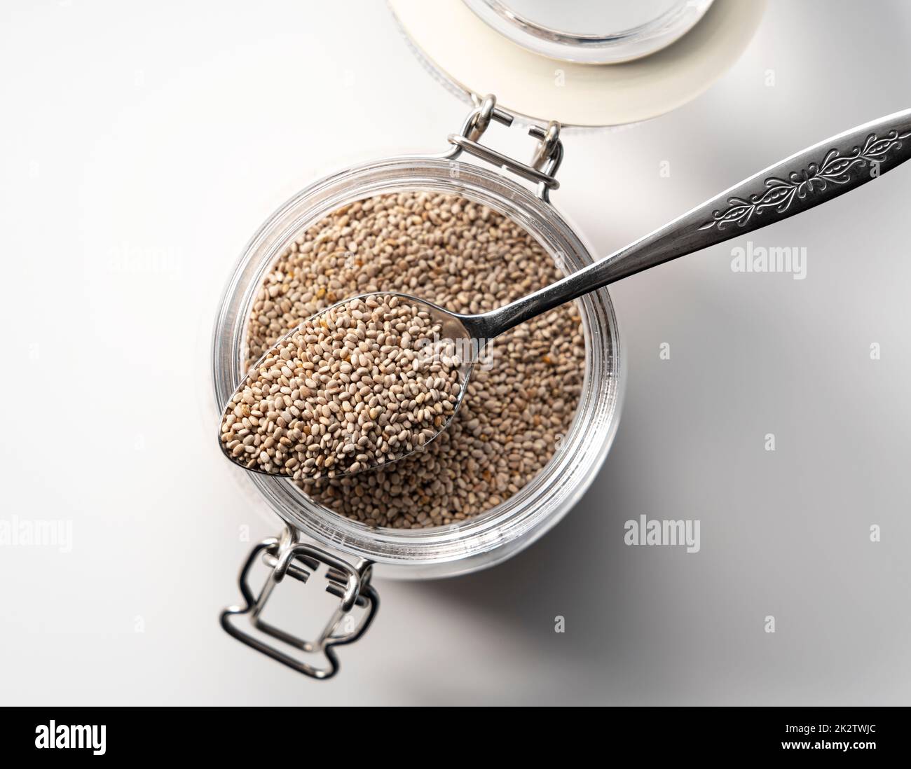 Contenant en verre avec cuillère et graines de chia blanc placées sur fond blanc. Banque D'Images