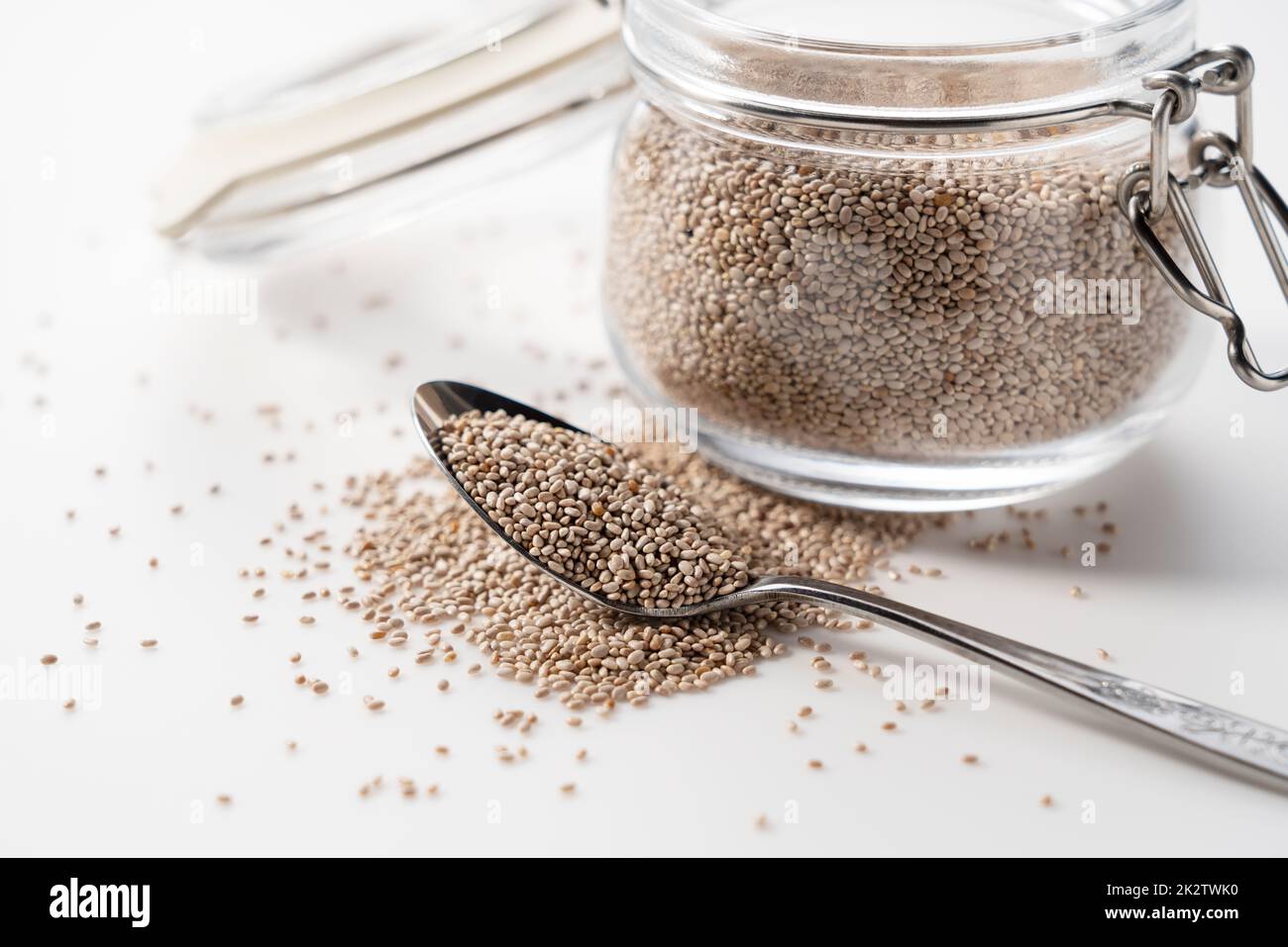 Contenant en verre avec cuillère et graines de chia blanc placées sur fond blanc. Banque D'Images