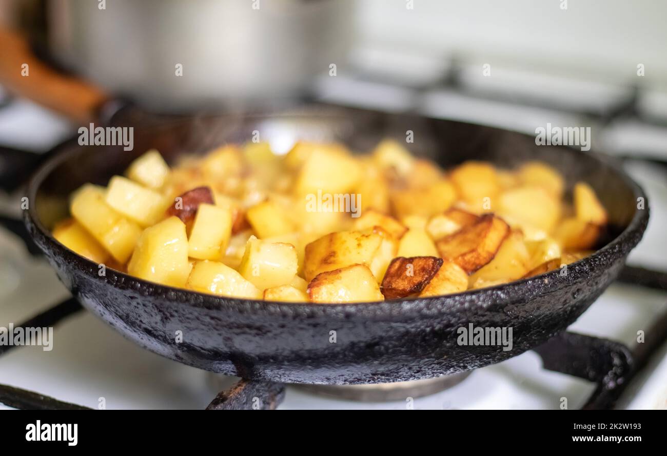 Rôtir les pommes de terre fraîches dans une poêle en fonte avec de l'huile de tournesol. Une vue sur une cuisinière avec une poêle remplie de pommes de terre frites dorées dans une vraie cuisine. Aliments cuits dans une poêle maison. Banque D'Images