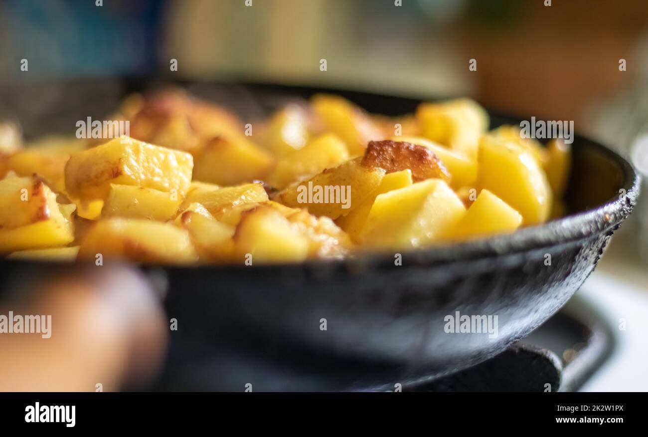 Rôtir les pommes de terre fraîches dans une poêle en fonte avec de l'huile de tournesol. Une vue sur une cuisinière avec une poêle remplie de pommes de terre frites dorées dans une vraie cuisine. Aliments cuits dans une poêle maison. Banque D'Images