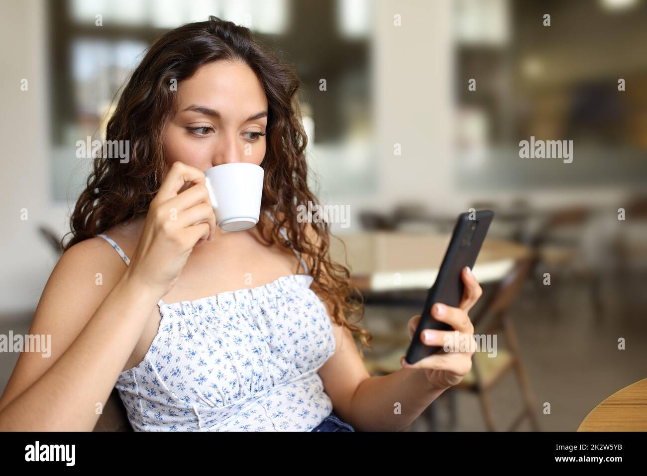 Femme buvant du café et regardant le téléphone dans un bar Banque D'Images