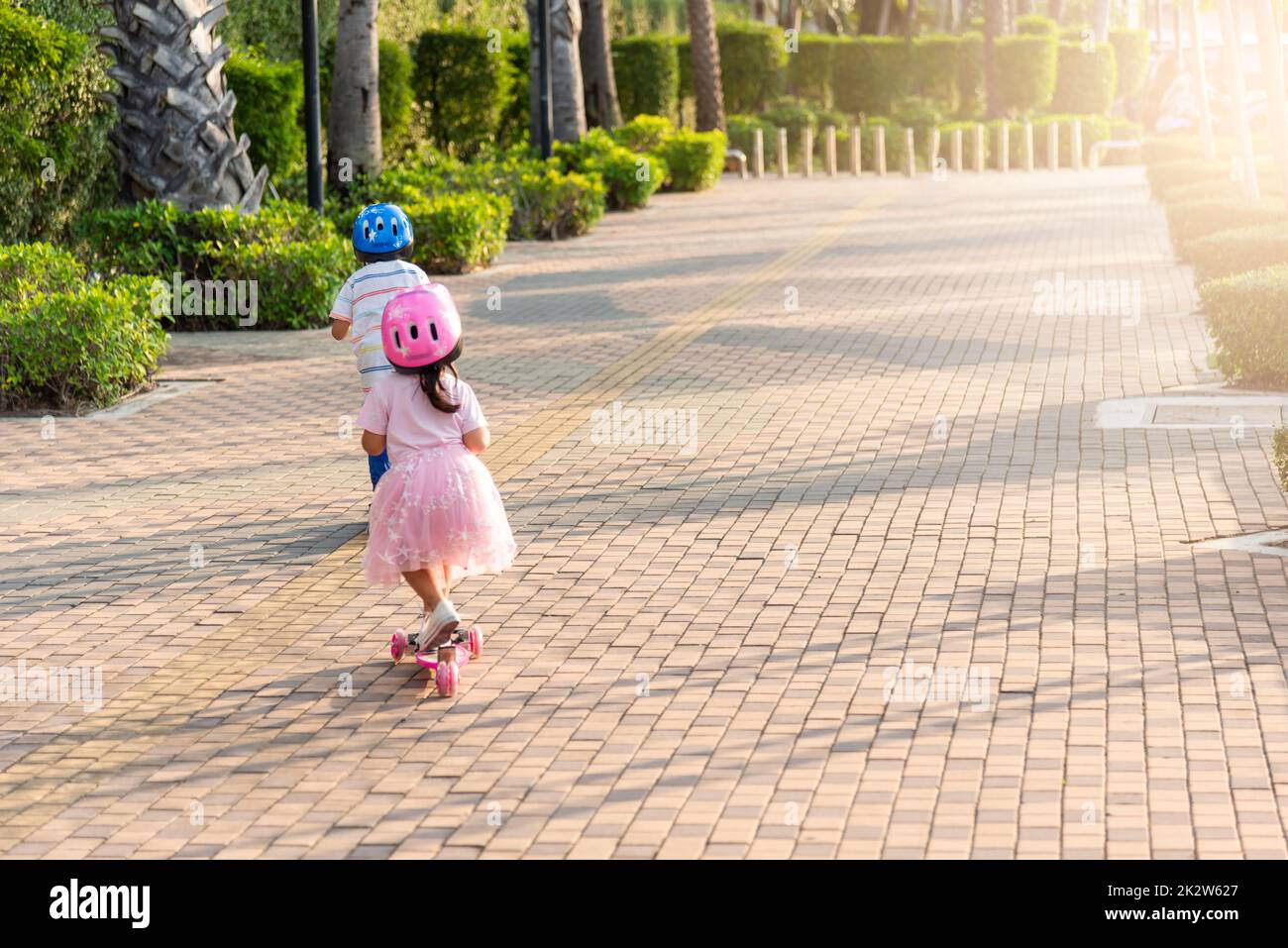 Retour asiatique petit garçon et fille porter un casque sûr jouer kick board sur la route dans le parc à l'extérieur le jour de l'été Banque D'Images