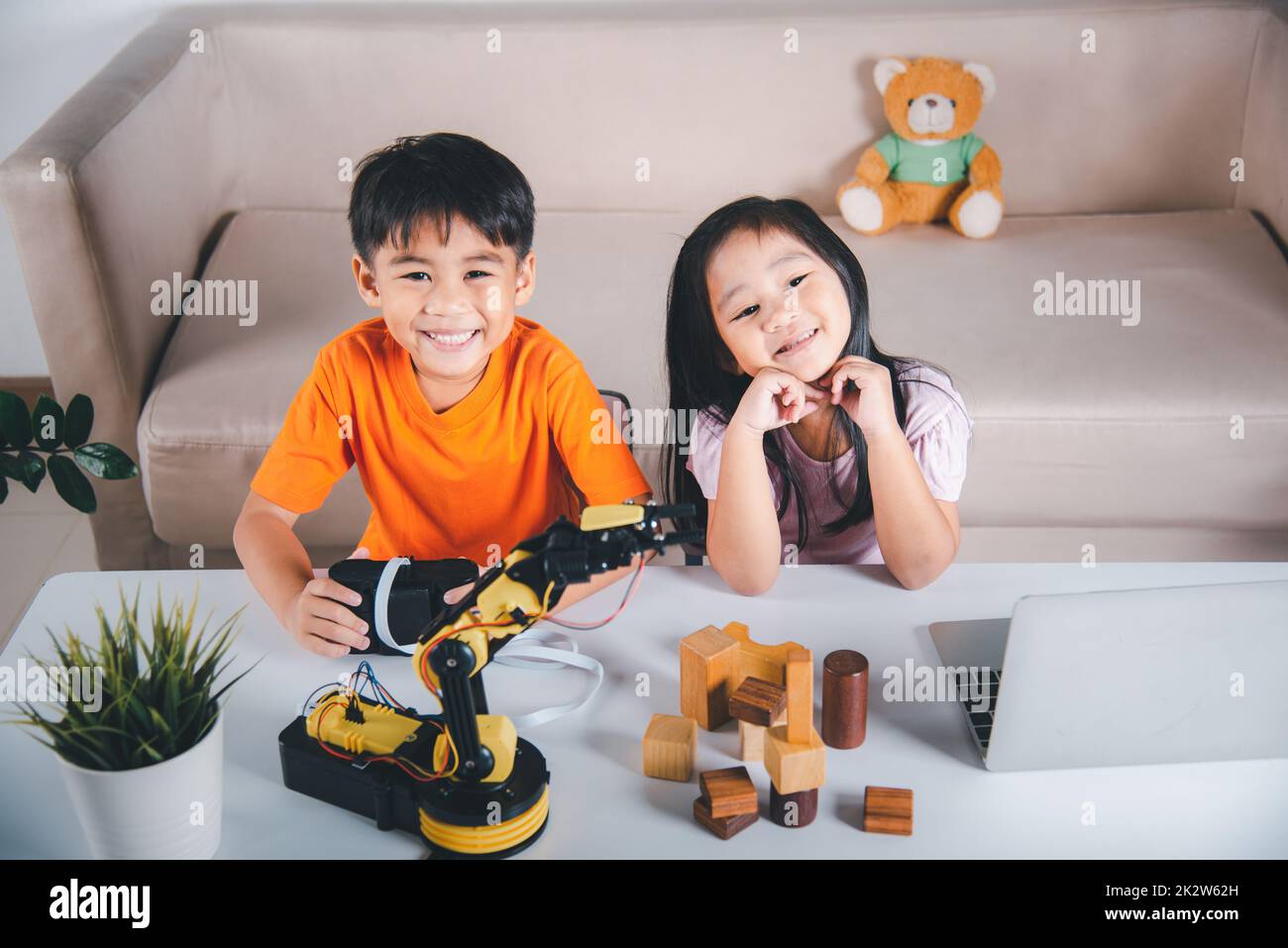 Kid Little girl programme code au robot avec ordinateur portable et le garçon test avec la télécommande pour ramasser le bloc de bois Banque D'Images