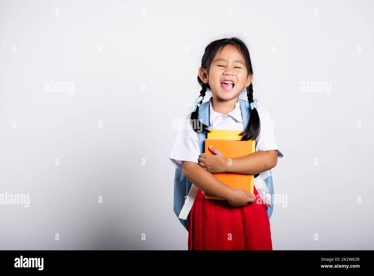 Asiatique adorable tout-petit souriant Happy Wear étudiant thaïlandais uniforme rouge jupe stand tenir ou serrer livre Banque D'Images