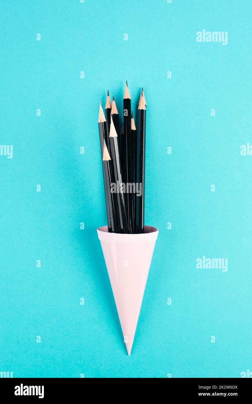 Crayons noirs dans un cône sur fond bleu, minimalisme, créatif, surréaliste et concept d'éducation, espace de copie pour le texte, mur de couleur pastel Banque D'Images