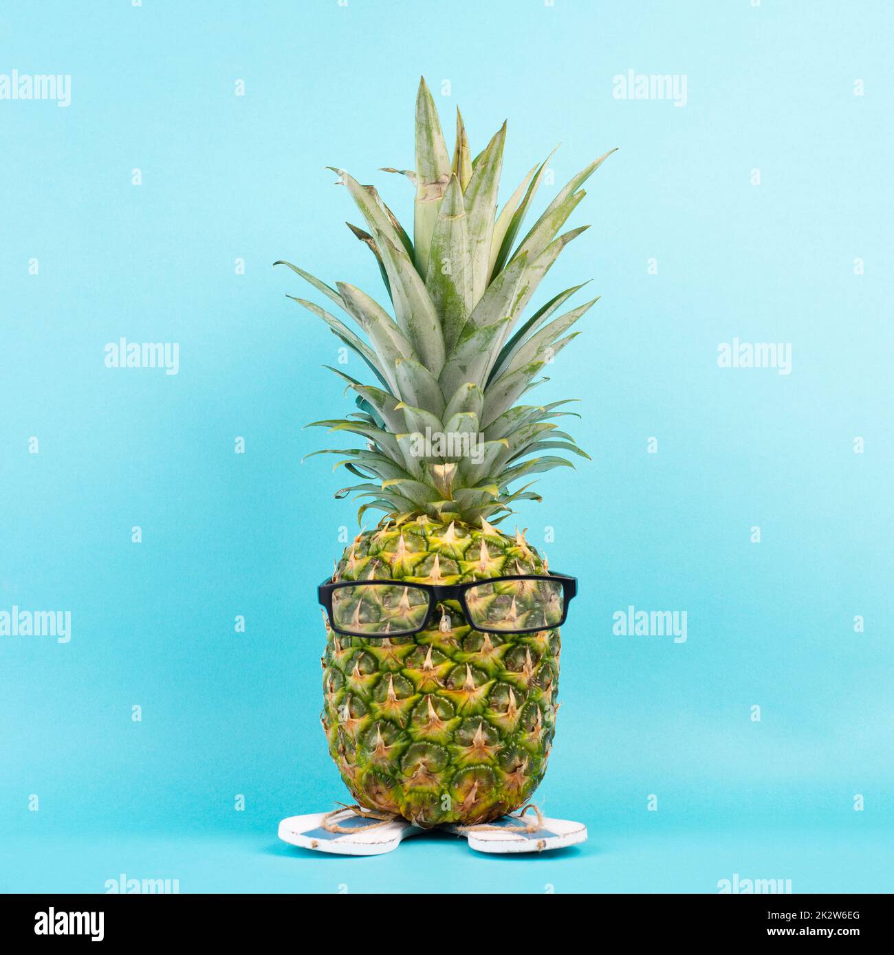 Ananas avec verres et tongs, concept de vacances et de voyage, vacances tropicales d'été, fruits drôles, fond bleu Banque D'Images