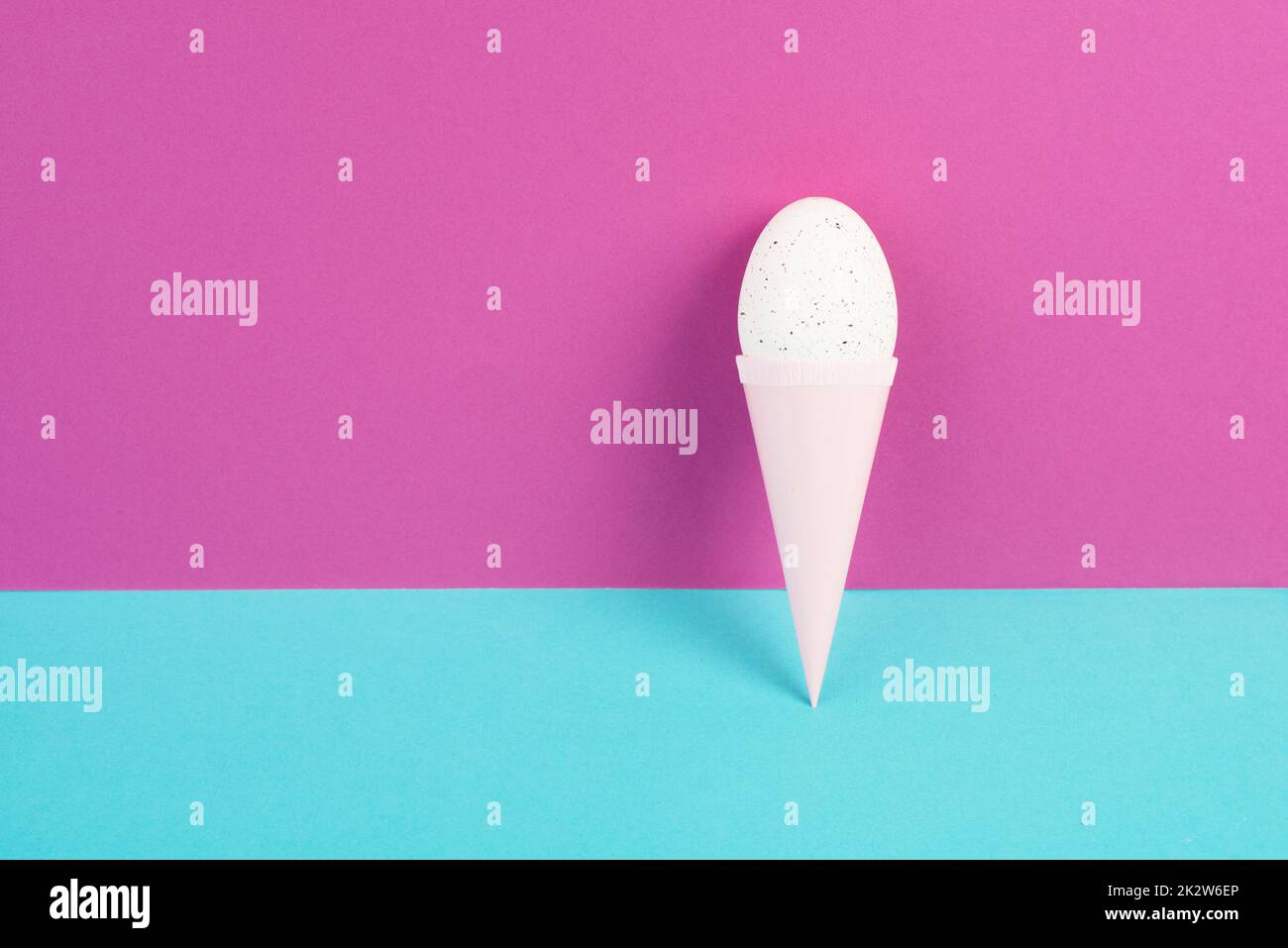 Cône de crème glacée avec un oeuf, fond rose et bleu, espace de copie, vacances de pâques, saison d'été, concept minimaliste et créatif, carte de voeux Banque D'Images