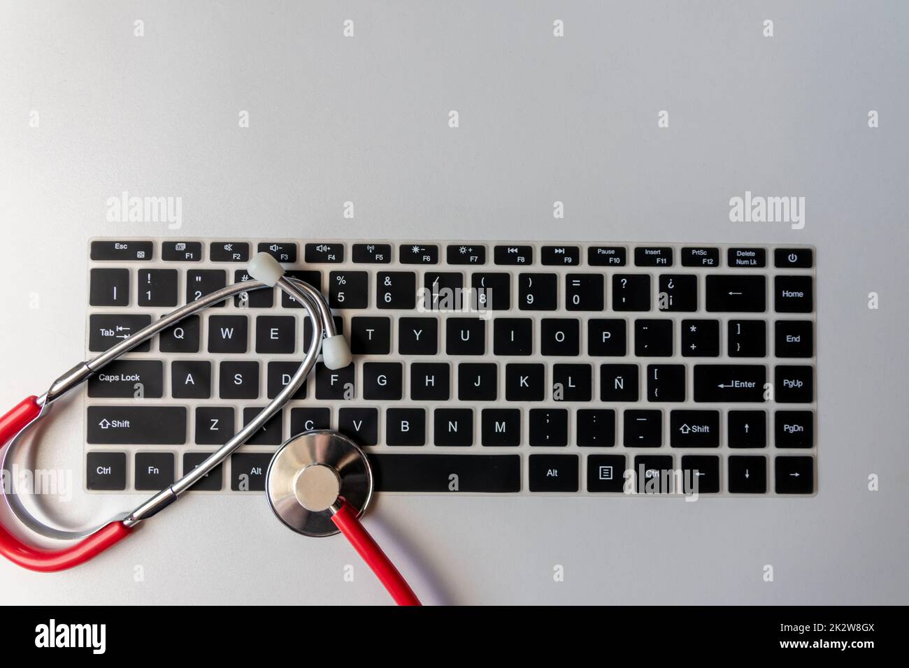 Stéthoscope rouge sur le clavier noir de l'ordinateur sur le bureau blanc montre le bureau numérique des médecins avec des dossiers numériques des patients pour le diagnostic médical et la mesure de cardiologie avec l'antivirus de contrôle hacker attaque Banque D'Images