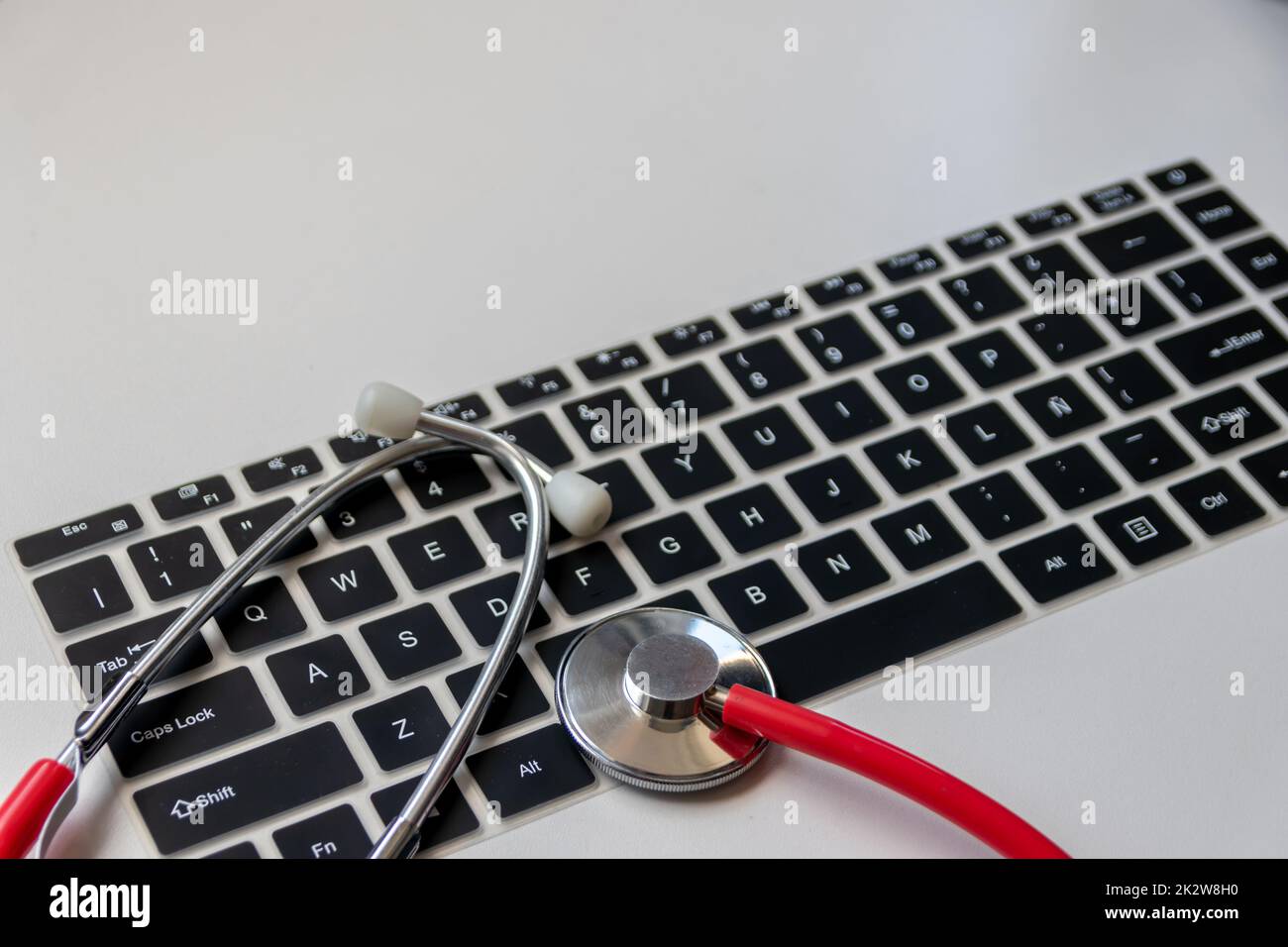 Stéthoscope rouge sur le clavier noir de l'ordinateur sur le bureau blanc montre le bureau numérique des médecins avec des dossiers numériques des patients pour le diagnostic médical et la mesure de cardiologie avec l'antivirus de contrôle hacker attaque Banque D'Images