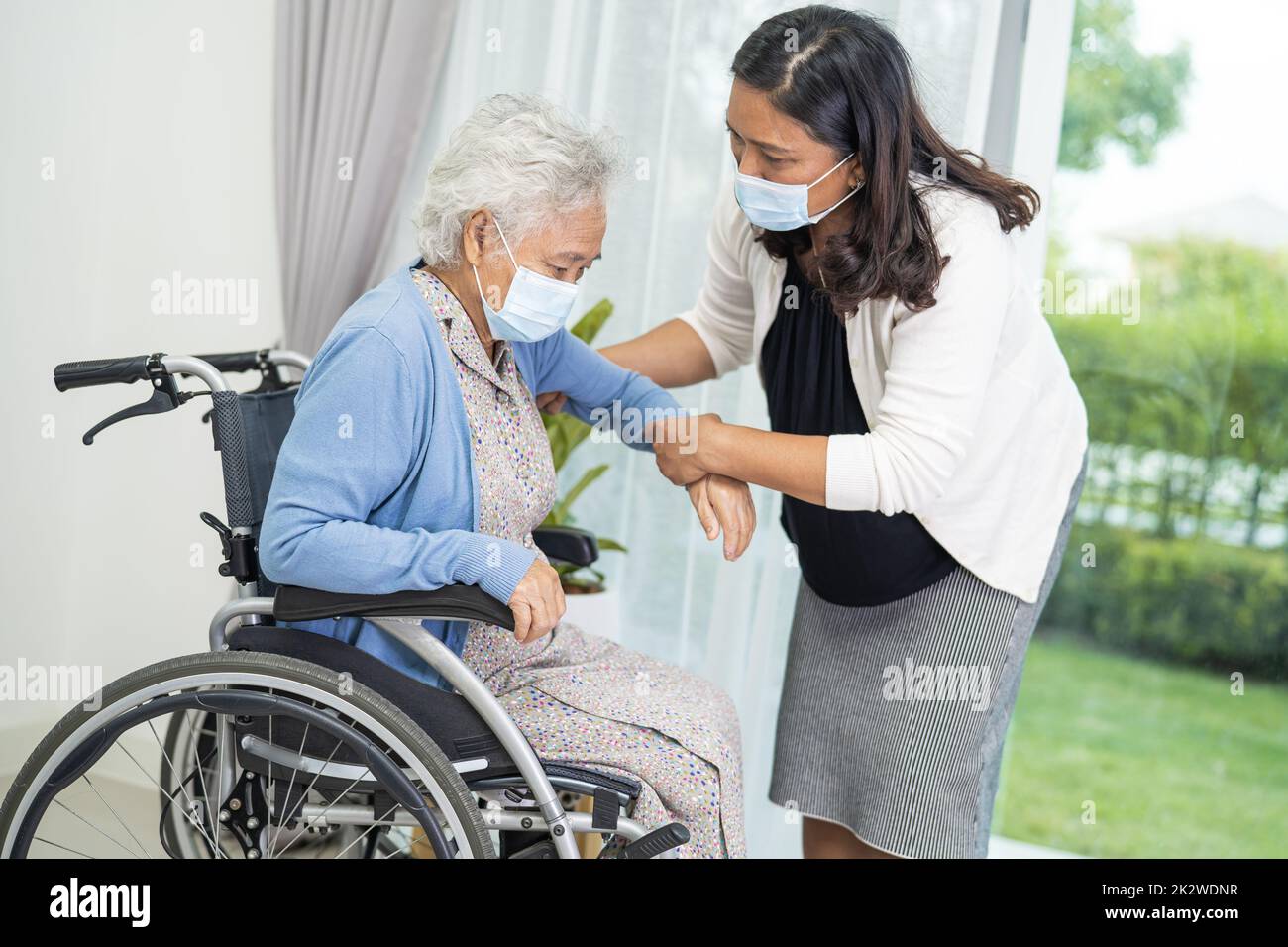 Aidez la vieille femme asiatique âgée assise sur un fauteuil roulant et portant un masque facial pour protéger l'infection à Covid-19 coronavirus. Banque D'Images