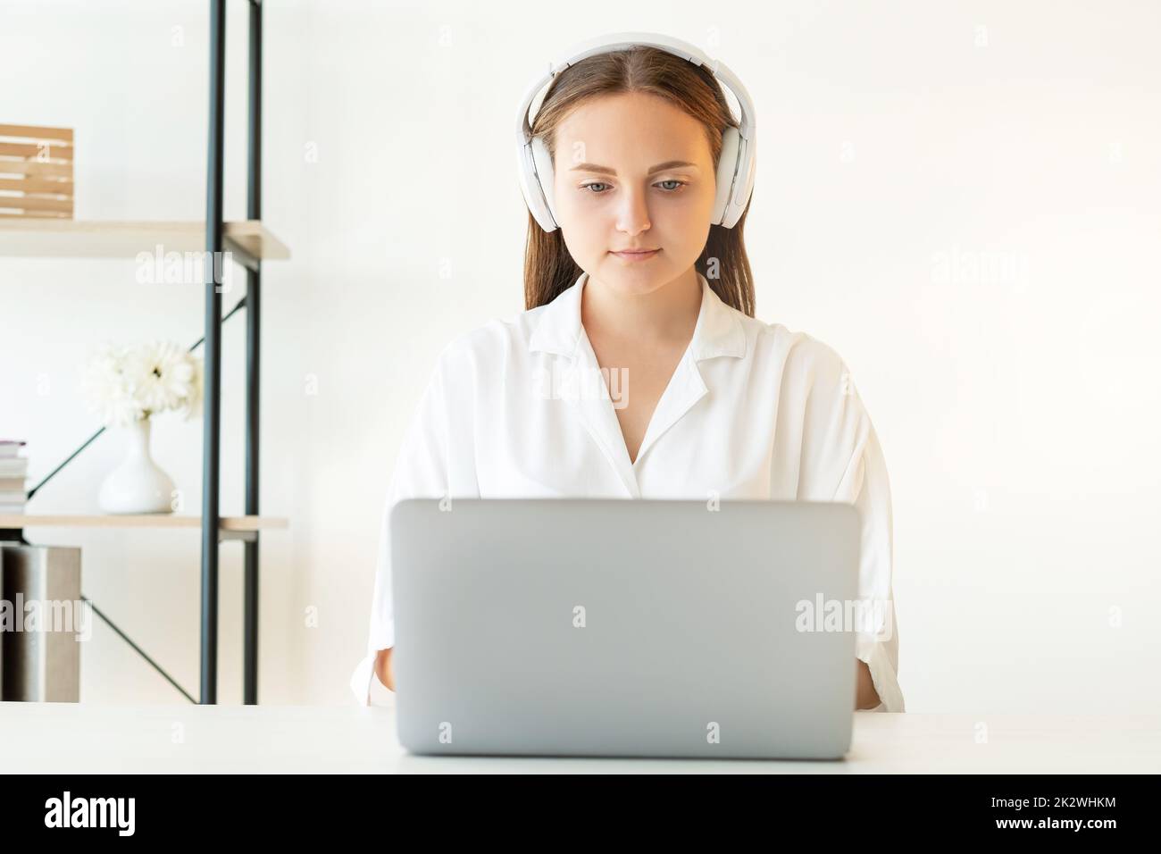 Formation en ligne. Enseignement à distance. Vidéo conférence. Réduction du bruit. Une femme intelligente et confiante dans un casque sans fil blanc travaillant à domicile avec un revers Banque D'Images