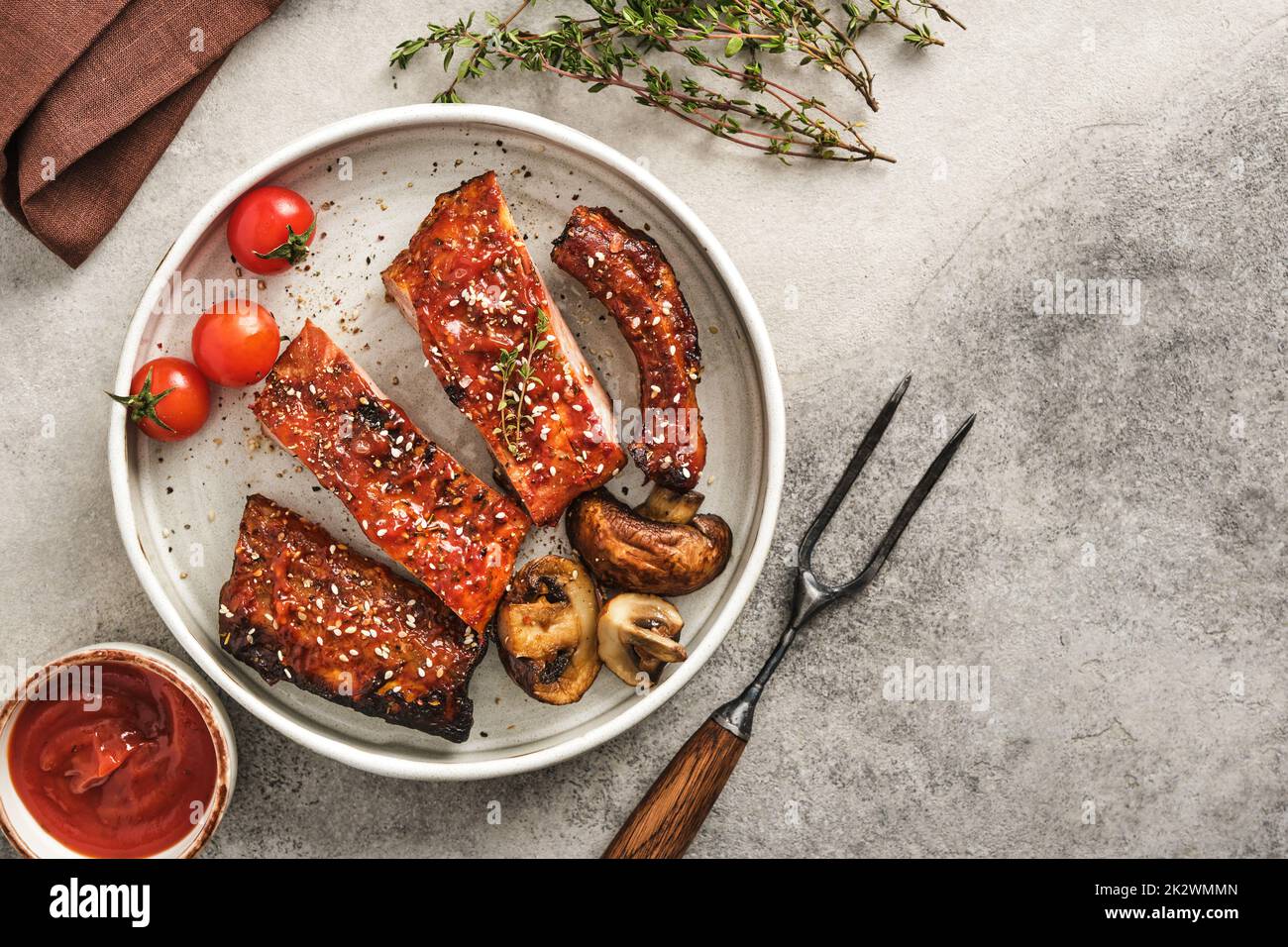 De délicieuses côtes grillées assaisonnées d'une sauce épicée et servies sur plaque avec des tomates cerises et des champignons. Banque D'Images