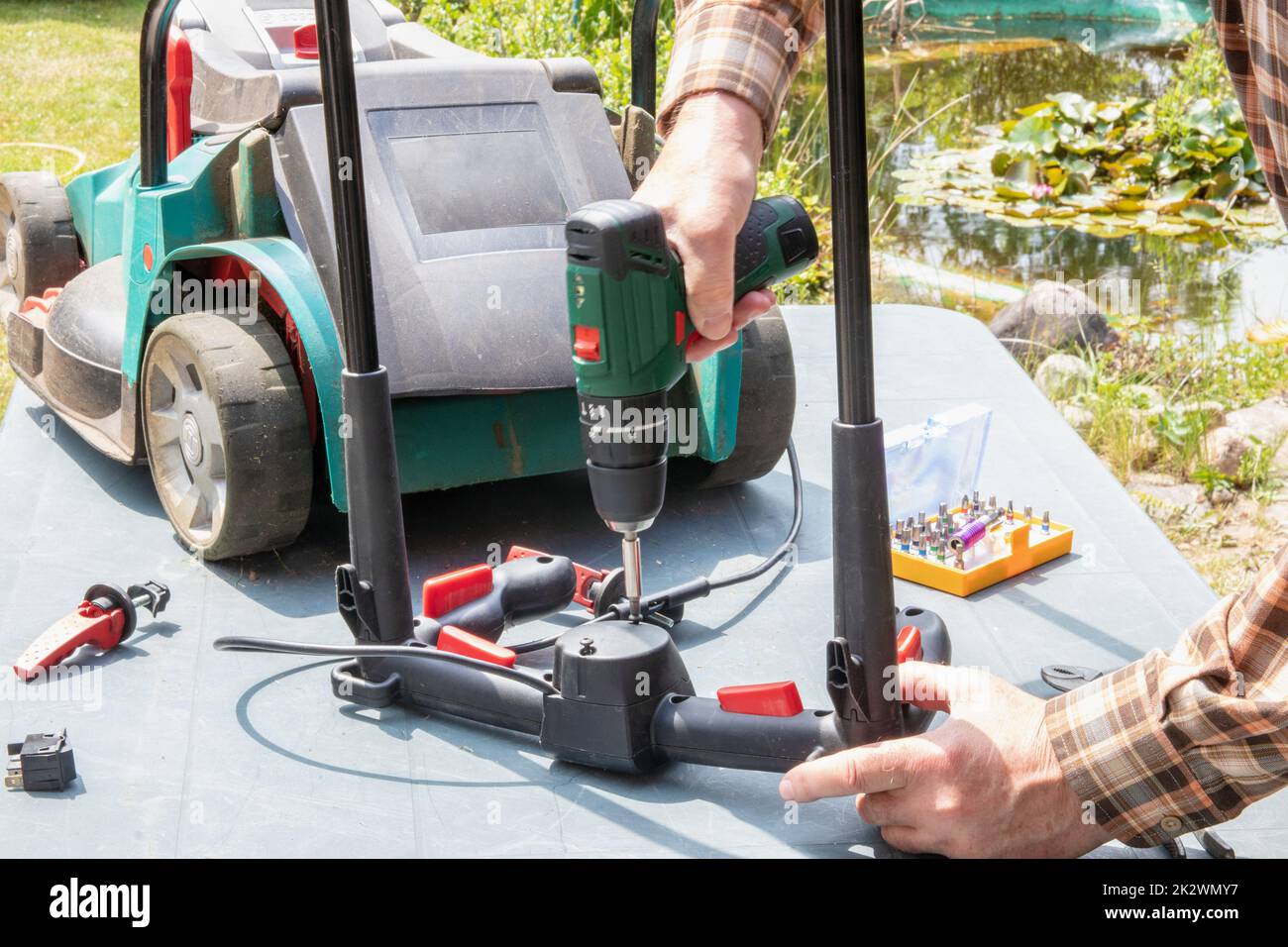 Un homme répare une tondeuse à batterie. L'interrupteur à bascule électrique pour démarrer le moteur est défectueux et doit être remplacé. Un artisan au travail. Banque D'Images