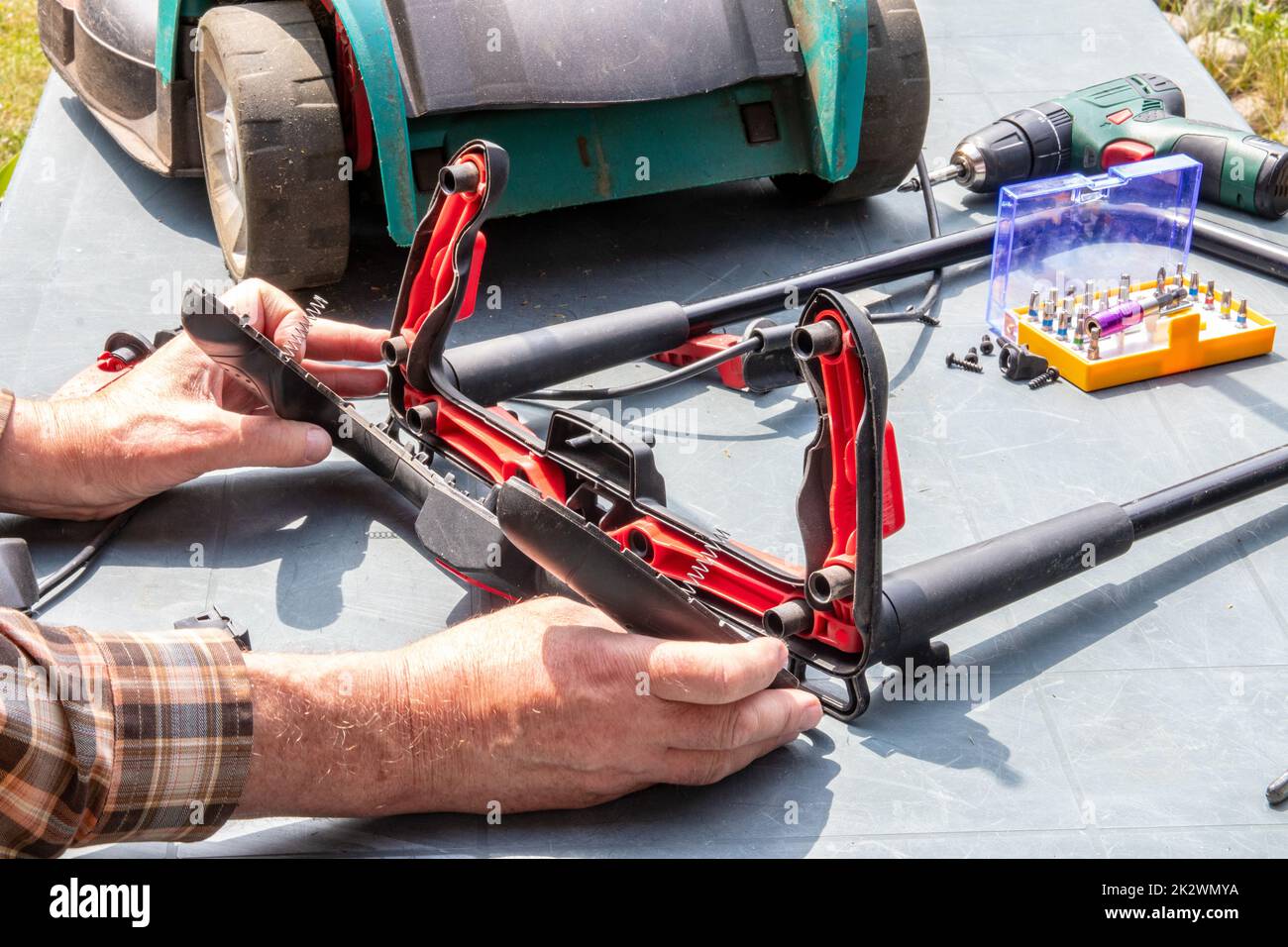 Un homme répare une tondeuse à batterie. L'interrupteur à bascule électrique pour démarrer le moteur est défectueux et doit être remplacé. Un artisan au travail. Banque D'Images