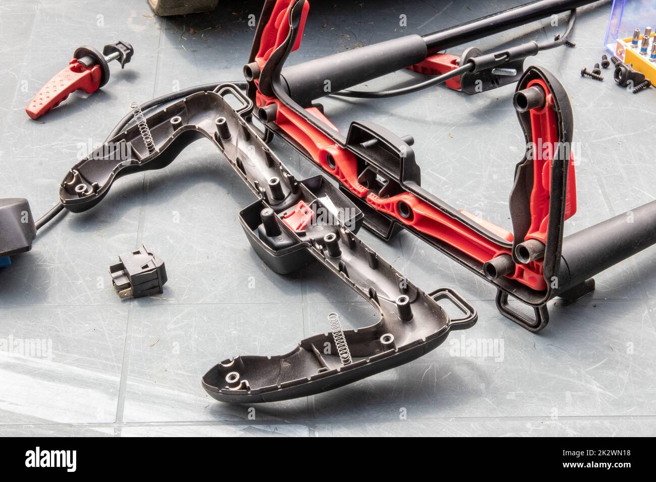 Un homme répare une tondeuse à batterie. L'interrupteur à bascule électrique pour démarrer le moteur est défectueux et doit être remplacé. Un artisan au travail. Banque D'Images
