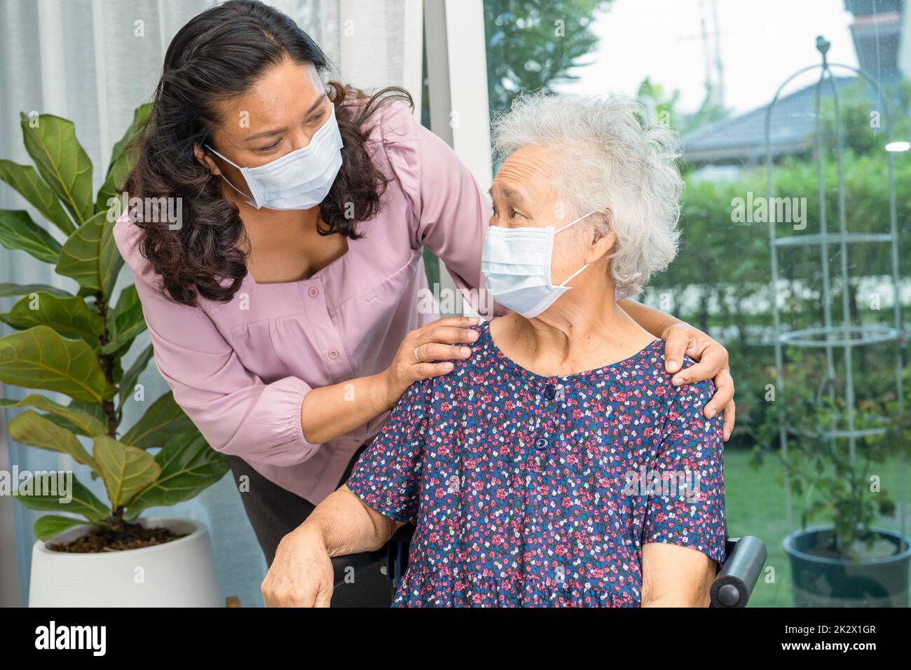 Aide-soignant asiatique senior ou âgée femme âgée assise sur un fauteuil roulant et portant un masque facial pour protéger l'infection Covid19 coronavirus. Banque D'Images