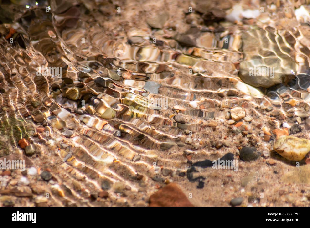 Pierres dans l'eau étincelante avec reflets ensoleillés dans l'eau d'une crique d'eau claire comme le fond naturel idyllique montre la méditation zen, de petites vagues et des ondulations soyeuses dans une source de montagne saine Banque D'Images