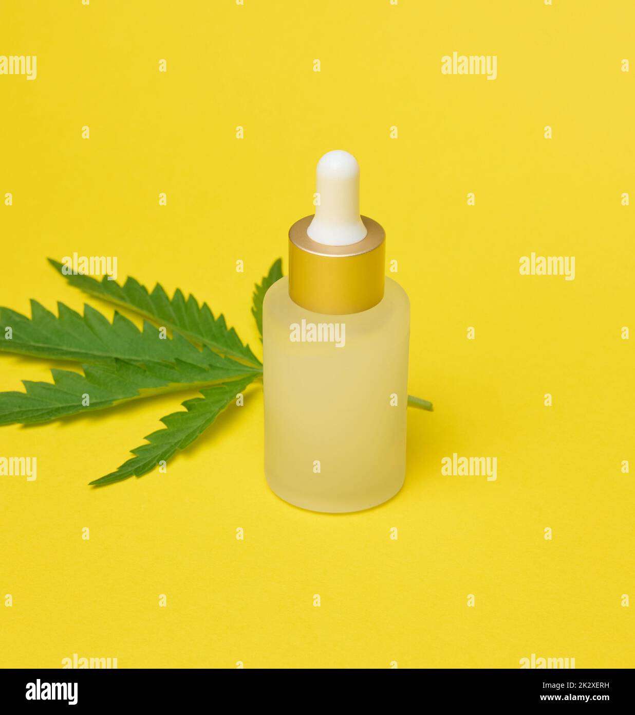 Flacon en verre blanc avec pipette et feuille de cannabis verte sur fond jaune Banque D'Images