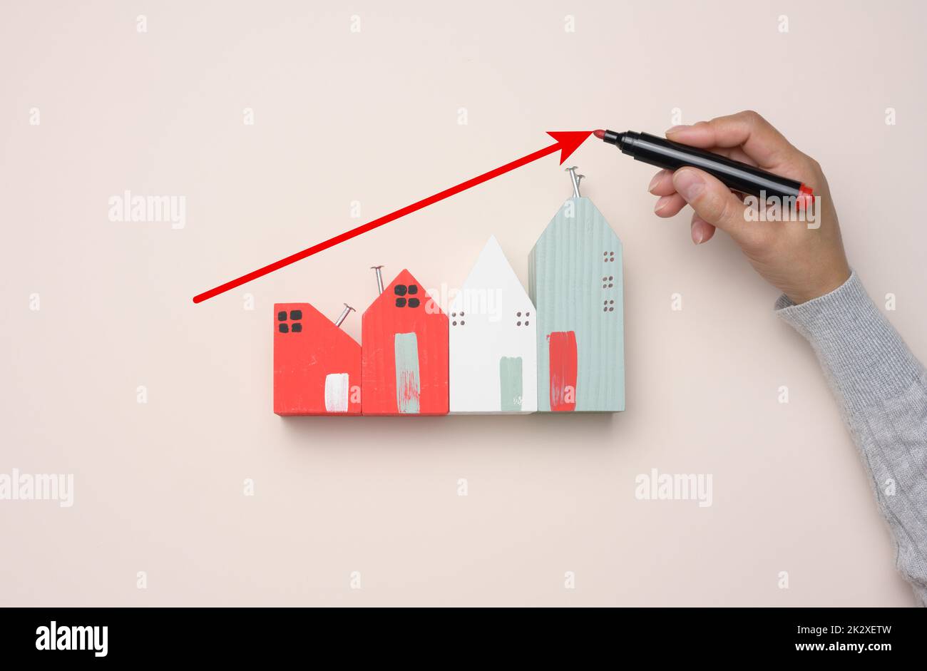 Une maison en bois miniature et une main de femme dessine un graphique avec des indicateurs de croissance. Banque D'Images