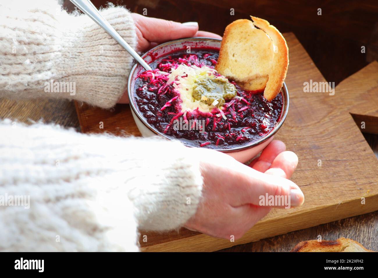 Mains de femmes tenant un bol de soupe de légumes avec betterave, fromage, crème aigre et pain sur fond de bois arustic . Banque D'Images