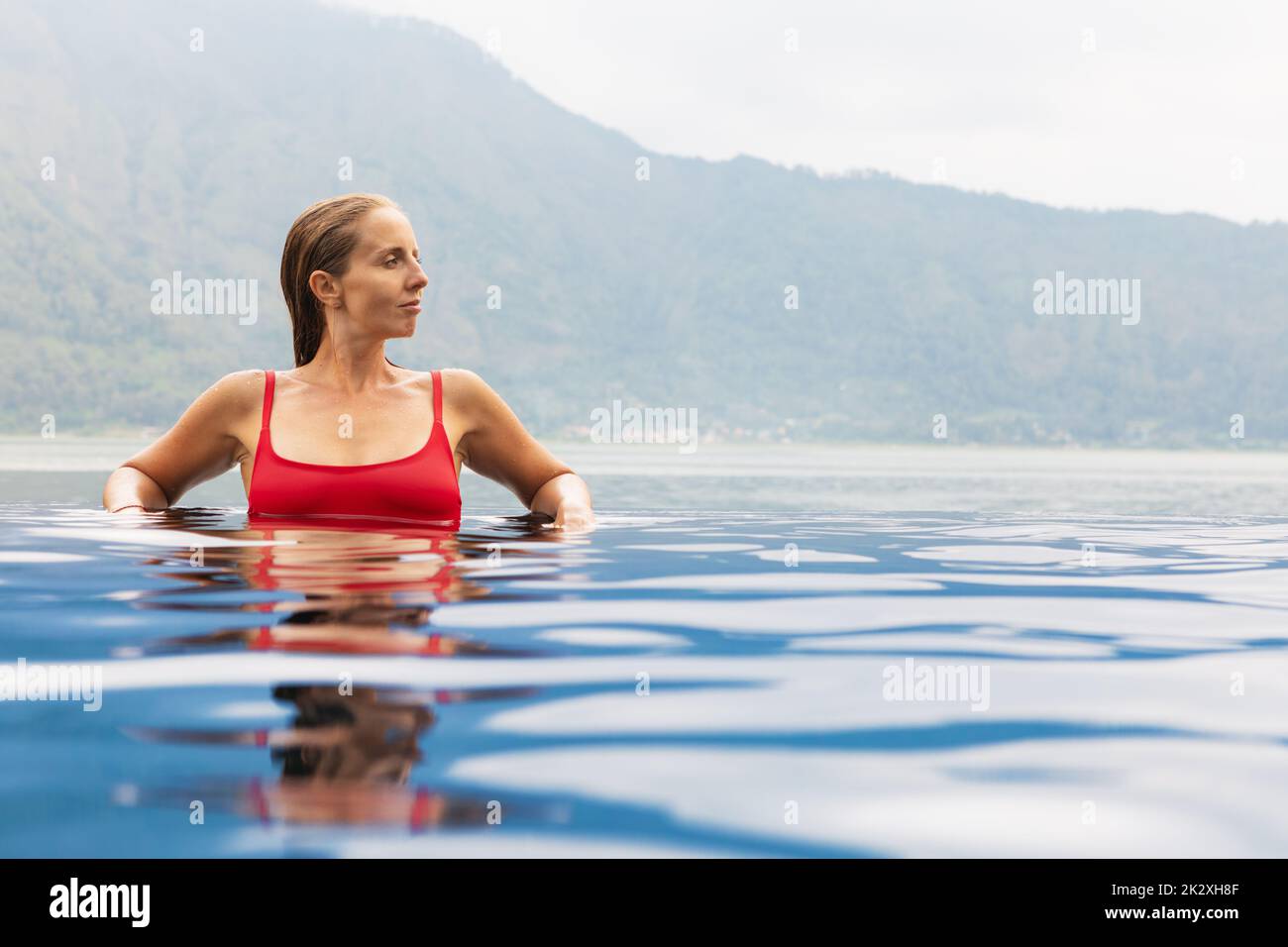 Une jeune femme se détende dans la piscine à débordement avec vue sur le lac. Spa naturel de source chaude sous le volcan Batur. Voyage à Kintamani, Bali. Un mode de vie sain Banque D'Images