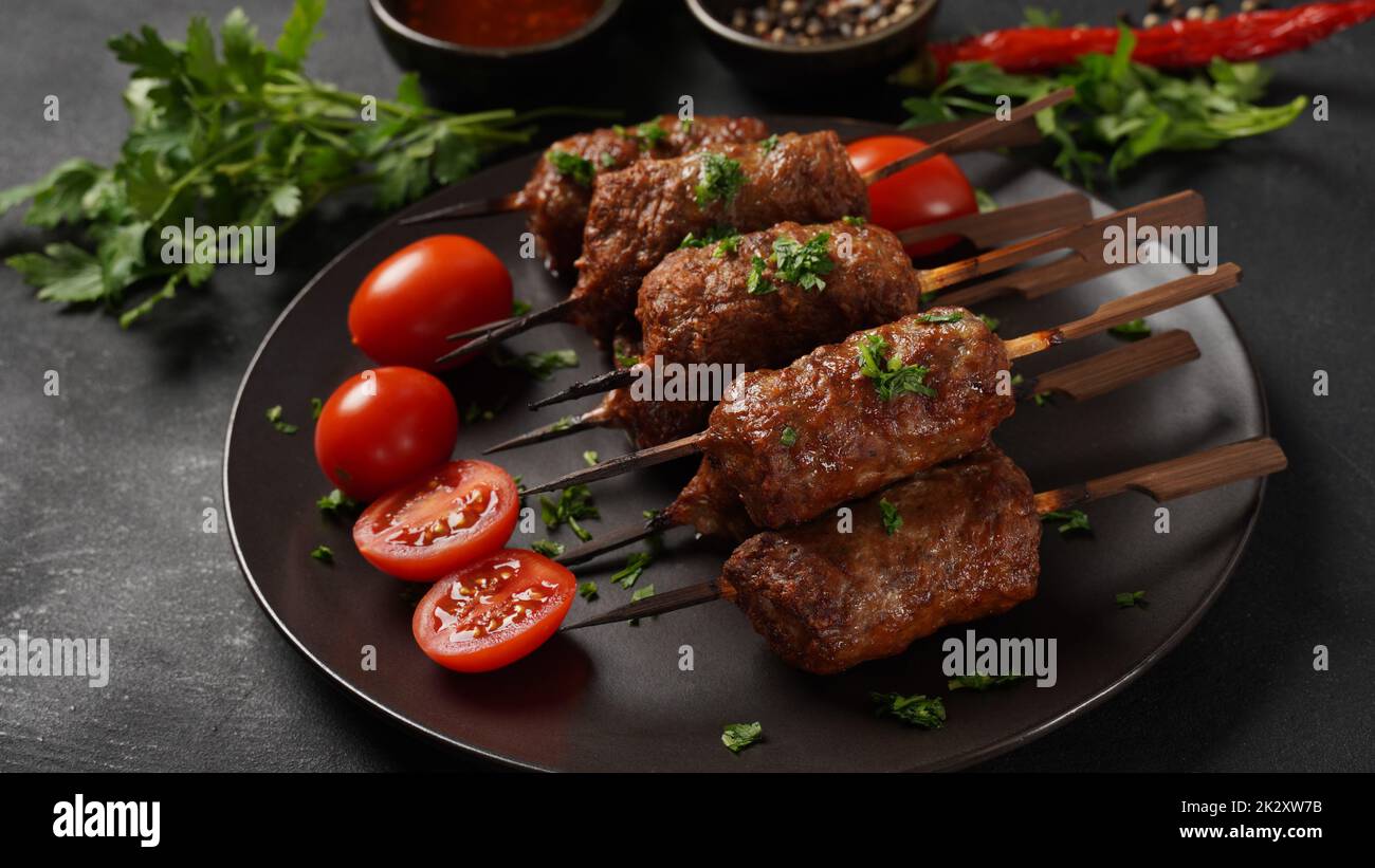 Le kebab shish est un repas populaire composé de cubes de viande brodés et grillés. Kebab de bœuf rôti sur une brochette de bois aux épices, aux herbes et aux tomates Banque D'Images