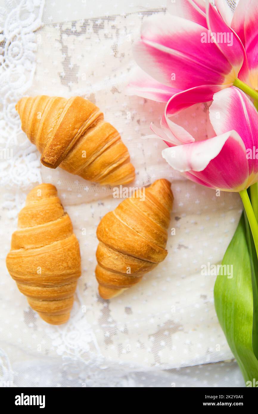 Trois croissants et de tulipes rose vif sur nappe en dentelle, close-up Banque D'Images