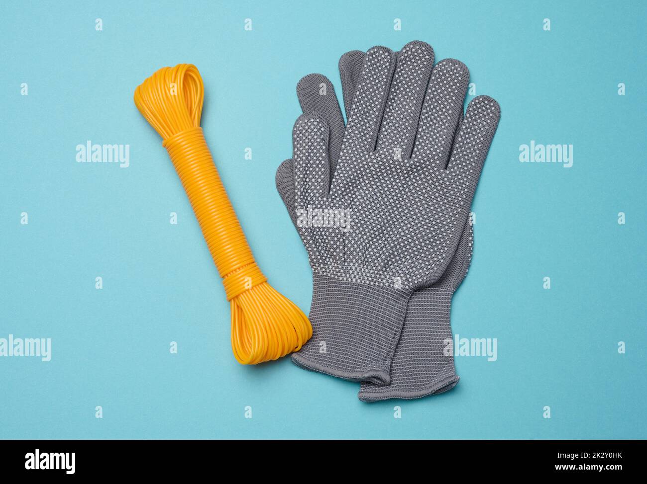 Une paire de gants de travail de protection en tissu gris et une corde orange sur fond bleu, vue du dessus Banque D'Images