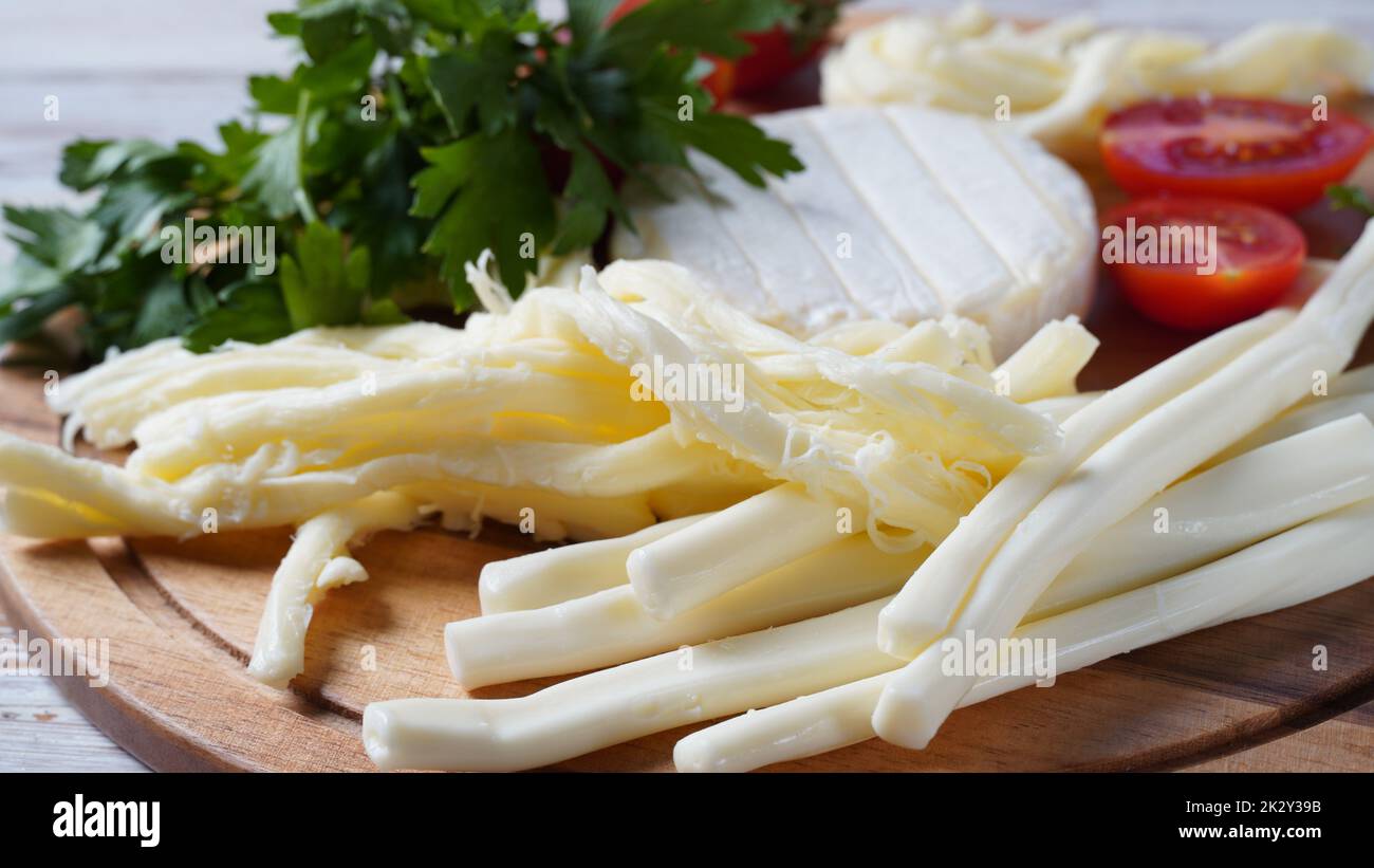 Camembert au fromage à cordes ou fouet au fromage - fromage en-cas salé avec tomates cerises et herbes sur la planche à découper. Banque D'Images