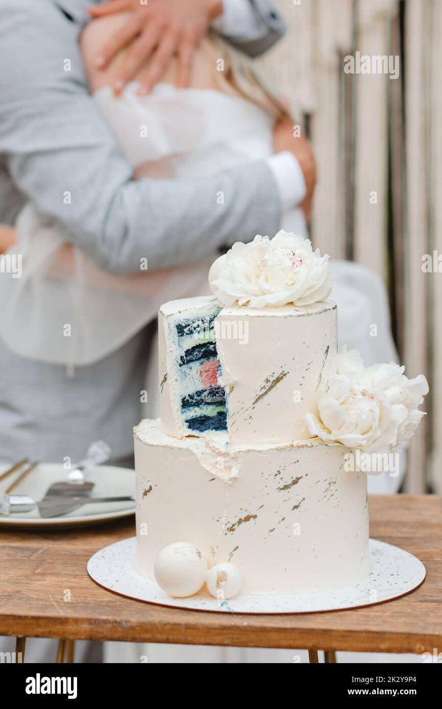 Un gâteau de mariage coupé avec un gâteau bleu et de la crème blanche, et en arrière-plan le marié encadre la mariée. Concept de parti de genre Banque D'Images