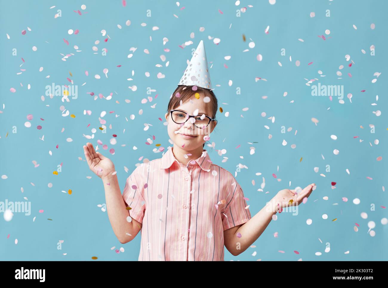 Taille vers le haut portrait pf fille ludique avec le syndrome de duvet appréciant la douche confetti à la fête sur fond bleu Banque D'Images