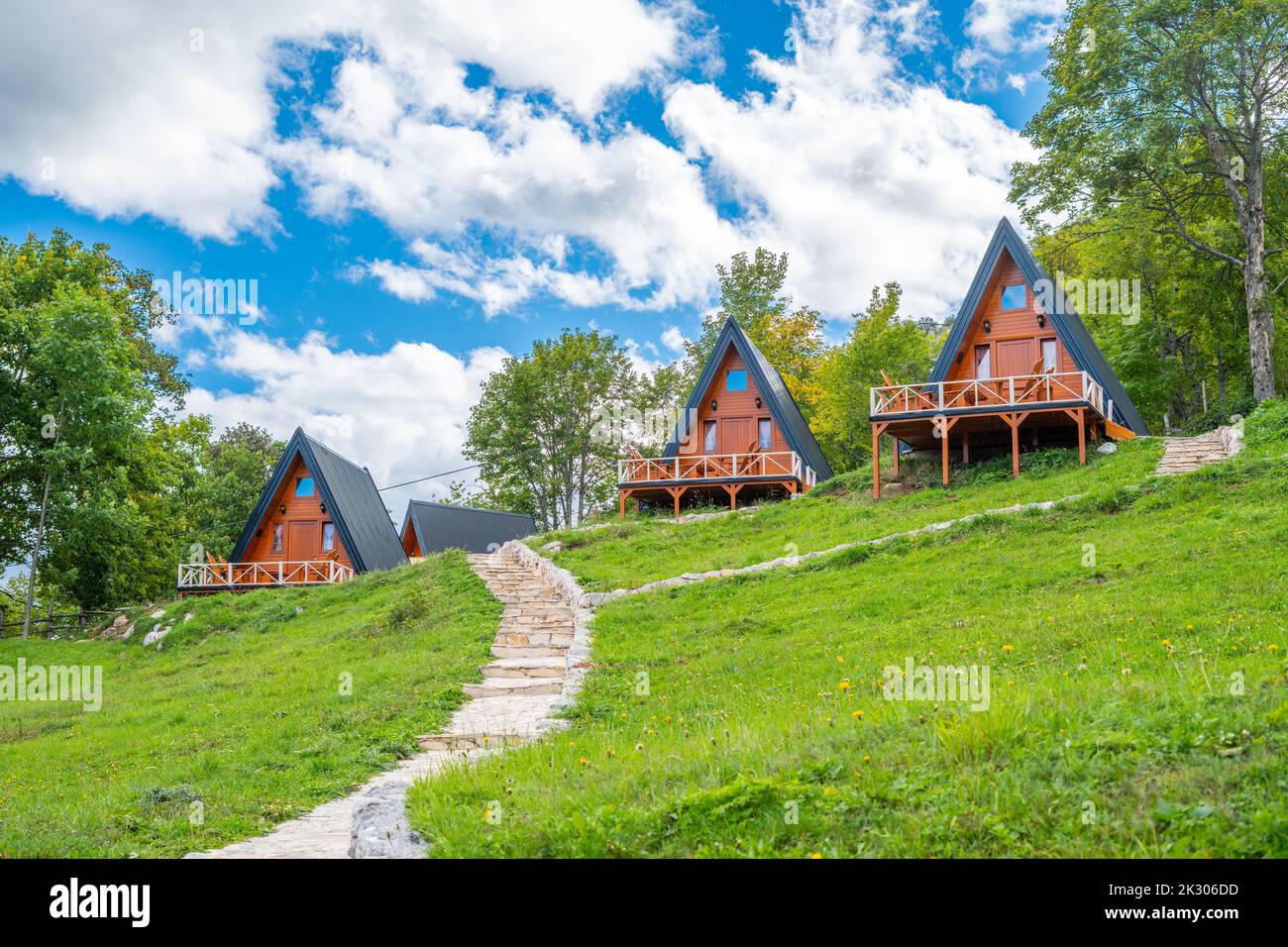 Trois nouvelles belles maisons de montagne en bois à cadre en a côte à côte avec des terrasses avec un chemin de pierre qui les mène et le ciel bleu et les nuages à l'arrière Banque D'Images