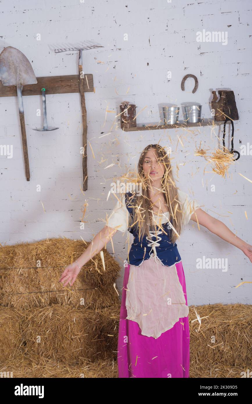 belle jeune femme, vêtue d'une tenue de fermier dans la grange jouant avec le foin le jetant sur son corps , métier de ferme Banque D'Images