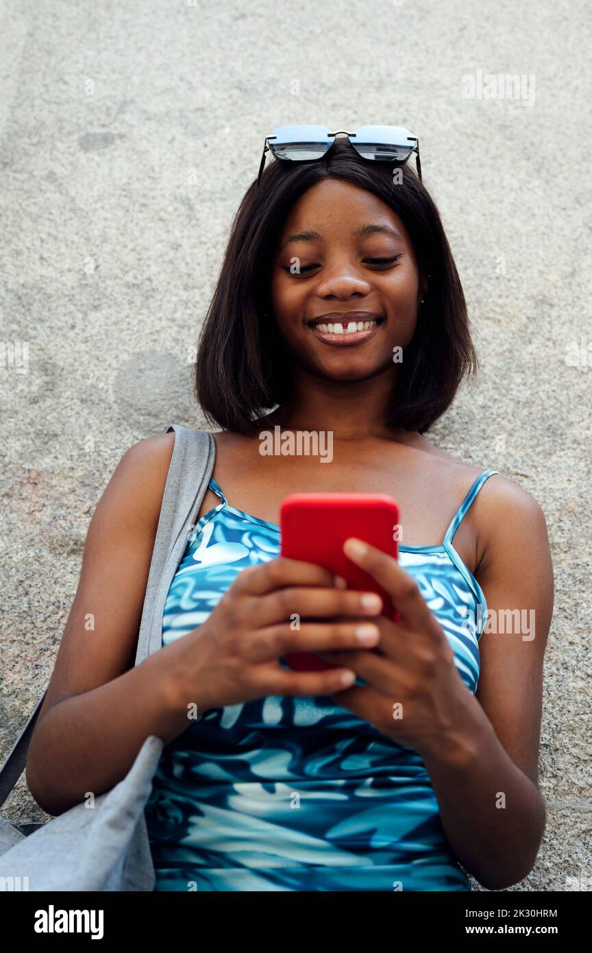 Message texte de femme souriante via un smartphone, devant le mur Banque D'Images
