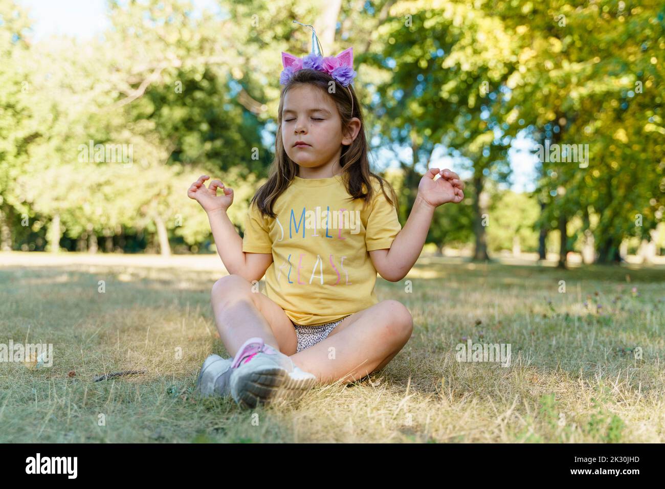 Fille pratiquant le yoga assis sur l'herbe au parc Banque D'Images