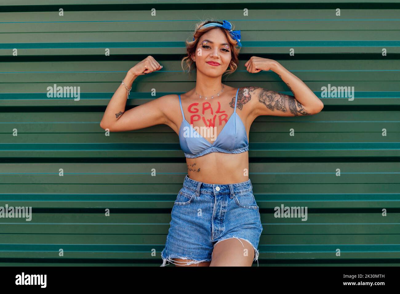 Femme avec le texte de puissance de fille sur la poitrine montrant les biceps devant le mur de métal vert Banque D'Images