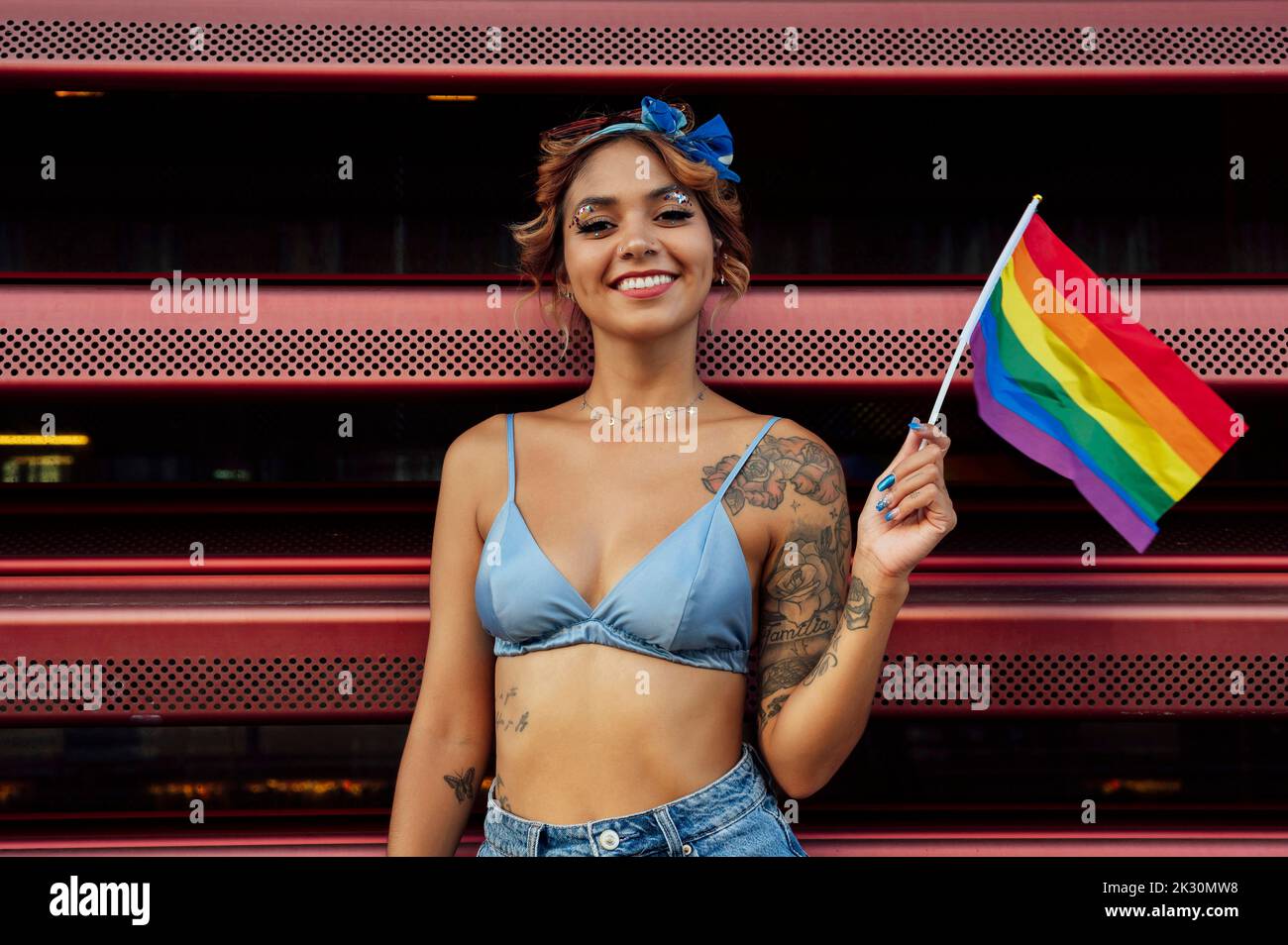 Femme tenant le drapeau arc-en-ciel devant l'obturateur Banque D'Images