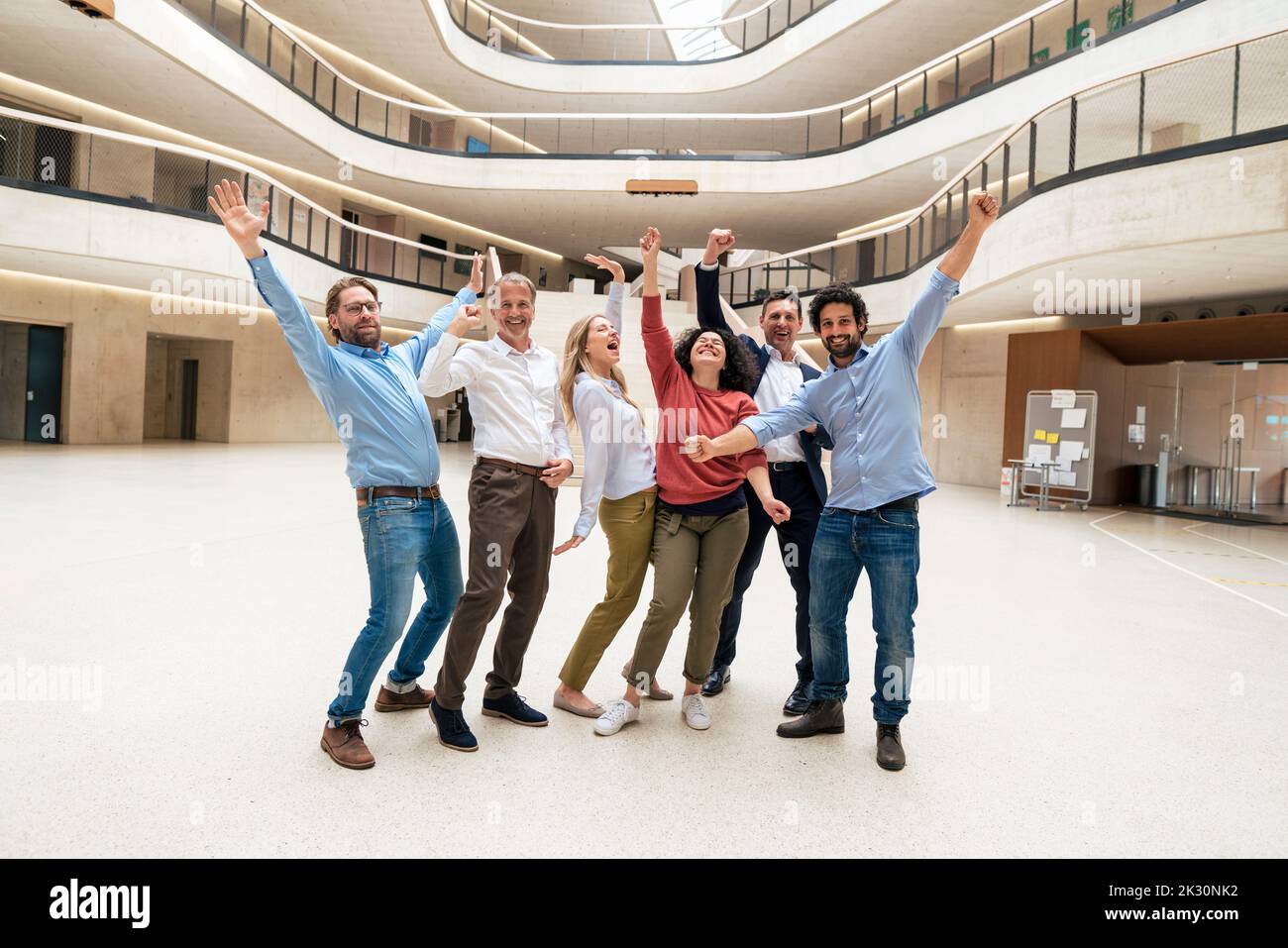 Des collègues d'affaires heureux avec des armes levées debout dans le hall Banque D'Images
