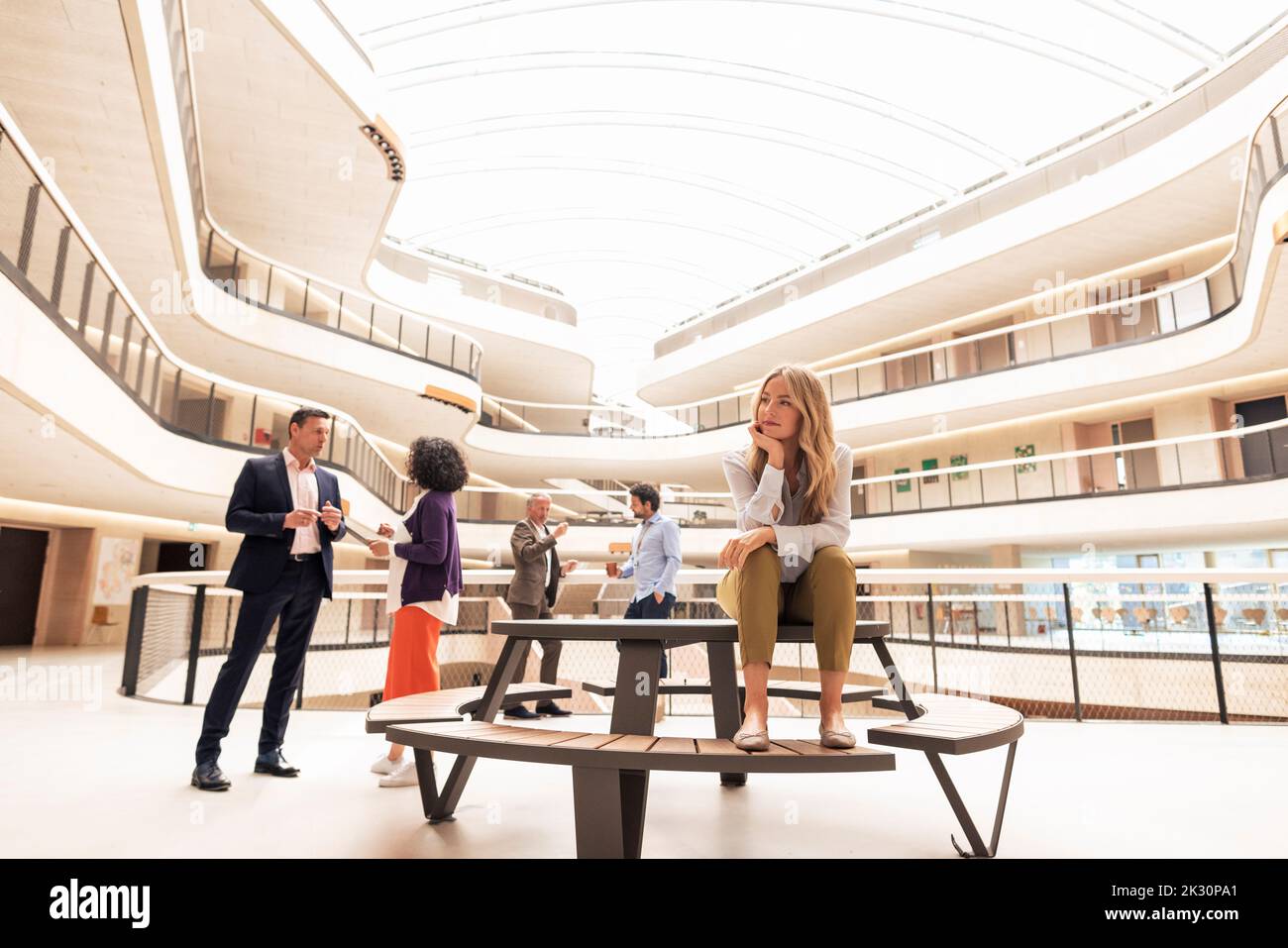 Femme d'affaires contemplative assise à table avec des collègues en arrière-plan Banque D'Images