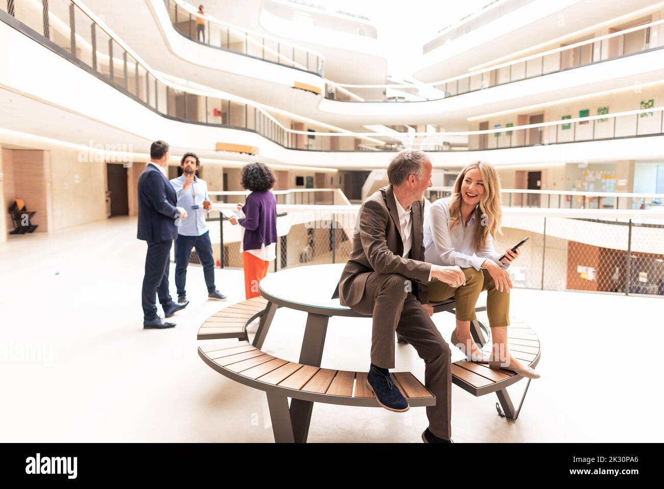 Homme d'affaires souriant et femme d'affaires discutant avec des collègues en arrière-plan Banque D'Images